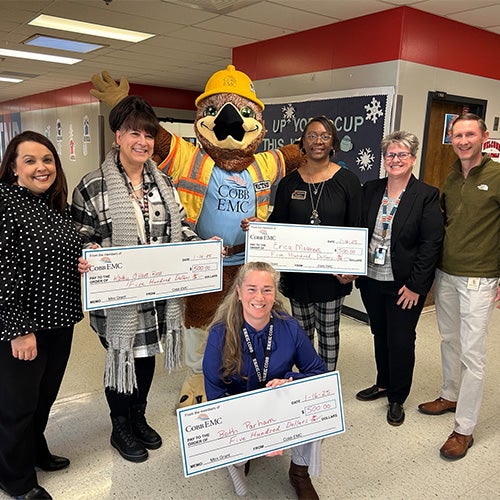 Teachers holding big checks inside a school with a hawk mascot