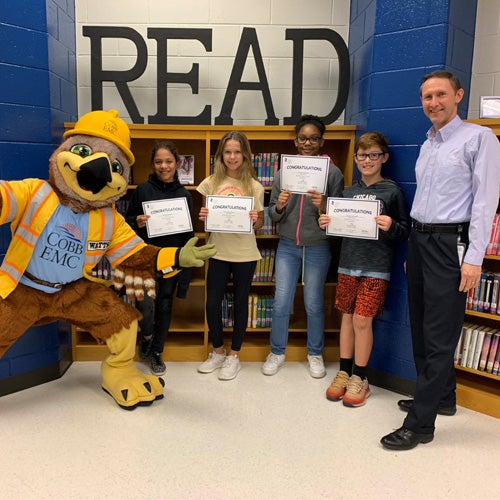 Mascot with employee and students holding certificates