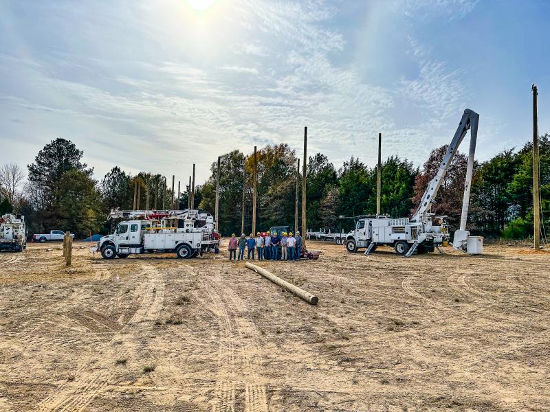 Cobb EMC linemen and trucks building power poles at a college